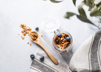 Homemade baked granola with nuts and fresh blueberry in a jar on a light background with napkin and branch. Healthy vegetarian muesli for breakfast.