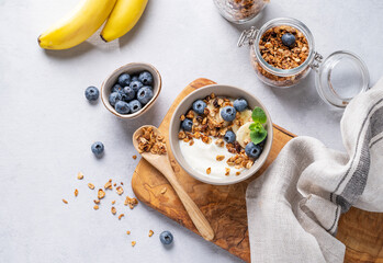 Homemade baked granola with yogurt, blueberries and banana in a bowl on a light background with fresh berries. Healthy vegetarian breakfast with muesli.