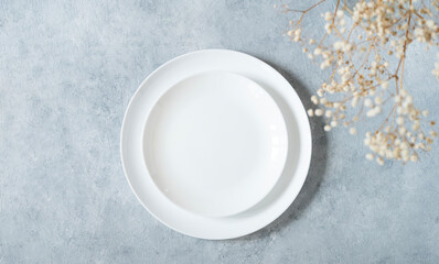 Table setting in a minimalist style with white plate and a bouquet of gypsophila on a blue background. Top view