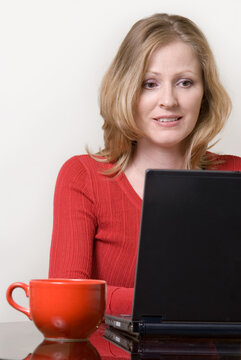 Attractive blond woman working in front of laptop computer wearing red with a big red coffee mug beside her