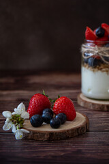 Glass jar with yogurt, granola and berries on dark background 