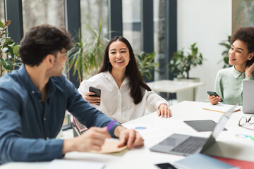 Three Diverse Coworkers Chatting Sitting At Table In Modern Office