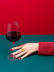 Gordijnen Cropped anonymous person in red clothes with well cared hand and manicured nails holding glass of wine over two color background. Wine shop, wine tasting, bar, wine list concept. Refreshment drink. © shyrokova