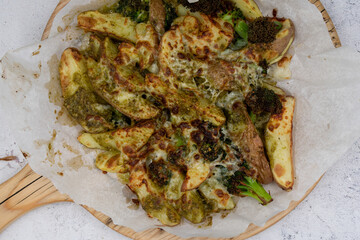 Air fried potatoes topped with cheese and pesto , on wooden board