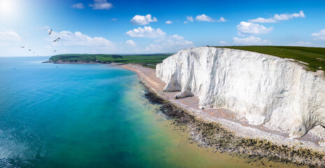 Panoramic aerial drone view of the famous Seven Sisters Chalk cliffs, Sussex, England, in early summer with sunshine and calm sea - obrazy, fototapety, plakaty