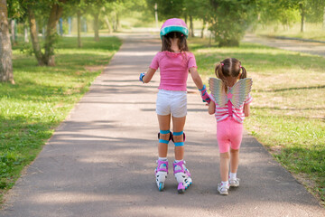 A little girl leads her older sister, who is learning to rollerblade, by holding her hand.  A child...