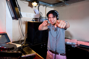 A Dj in a dj booth smiling and pointing at the camera