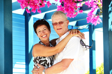 attractive mature couple posing under a pergola draped in flowers