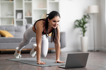 Beautiful athletic young woman have workout at home, using laptop