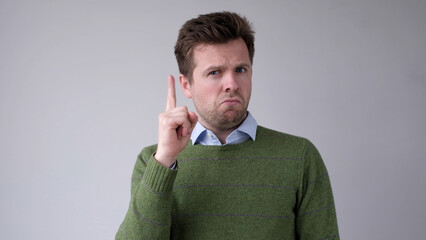 The serious European young man shows a finger up and gives advice or recommendation.