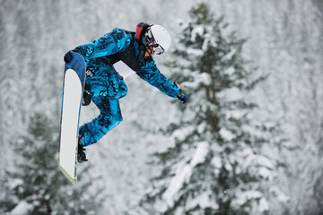 young boys jumping in air ind showing trick with snowboard at winter season