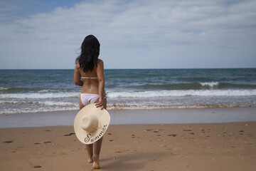South American woman, young and beautiful, brunette with bikini and hat with the word summer held...