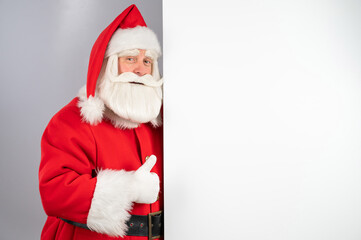Santa claus peeks out from behind an empty Christmas advertisement and shows a thumbs up.