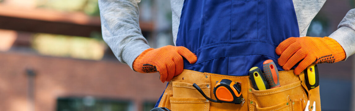 Male builder in blue overalls wearing tool belt. Close up on waist area
