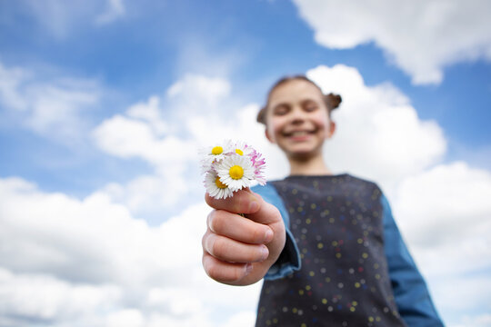 Little girl with bouquet of daisies in front of sky background