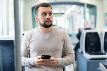 Interested young man browsing messages on phone on way to work in modern streetcar ..
