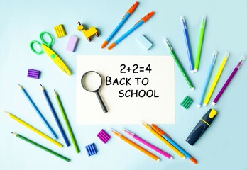 On a blue background, school supplies are scissors, pencils, felt-tip pens, a magnifying glass, plasticine, and a sheet of paper with the text back to school.  Education concept.  Flat lay.