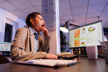 Tired corporate employee yawning in startup office after working overtime at financial strategy to...