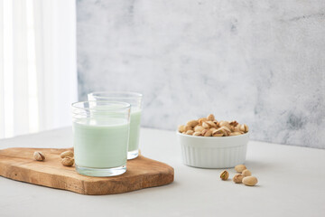 Glasses of homemade pistachio milk on a wooden board next to pistachios. The perfect drink for...