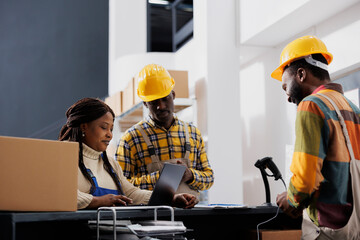 Post office employees making electronic invoice for customer parcel at reception counter desk. African american postal warehouse workers team checking delivery online schedule on laptop