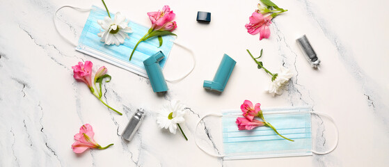 Asthma inhalers with medical masks and flowers on light background