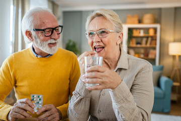 senior couple at home woman take medicine while her husband sit beside
