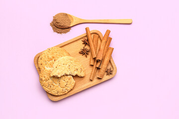 Wooden board with tasty cookies, cinnamon sticks, powder and anise stars on pink background