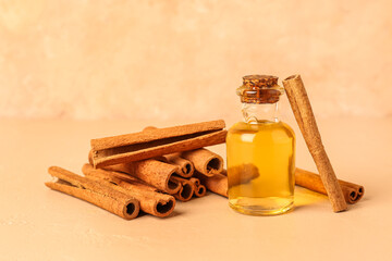 Bottle of essential oil and cinnamon sticks on color background