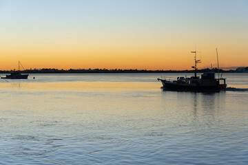 Commercial fishing boat leaving in morning light in silhouette