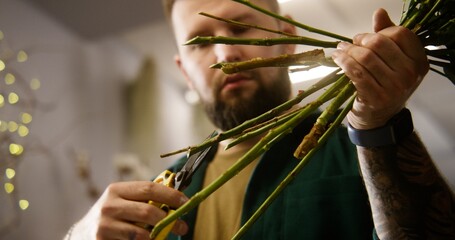 Close up shot of professional florist entrepreneur cutting the stems of fresh flowers using secateurs. Man creates beautiful bouquet to sale or delivery. Floral business and entrepreneurship concept.