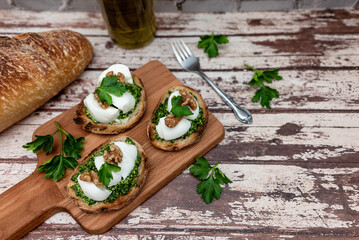 Tasty bruschetta with parsley pesto, mozzarella and walnuts. Bread on a wooden cutting board, top view.
