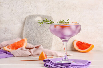 Glass of purple gin and tonic with grapefruits on light table