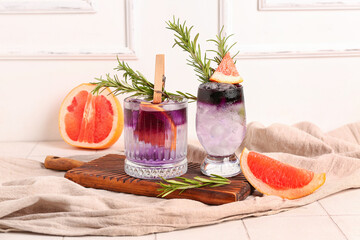 Glasses of purple gin and tonic with grapefruit and rosemary on white tile table