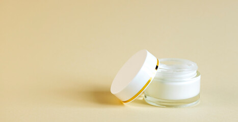 Opened round glass jar with cosmetic cream and lid next to it, on a beige background. Skin care concept.