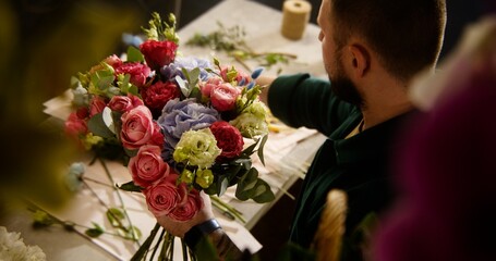 Male professional florist, entrepreneur, seller collects bouquet and makes composition of fresh flowers for customer in flower shop. Concept of floristry, floral small business and entrepreneurship.