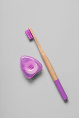 Dental floss and purple bamboo toothbrush on grey background
