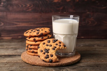 Glass of milk and tasty cookies with chocolate chips on wooden background