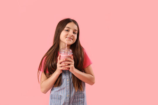 Little girl with glass of smoothie on pink background