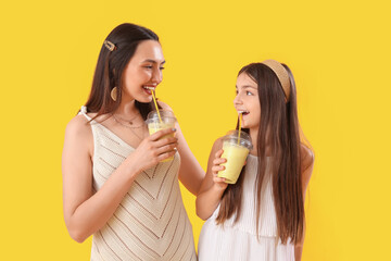 Little girl with her mother drinking smoothie on yellow background