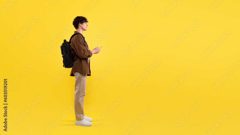 Poster student guy using smartphone pointing finger aside over yellow background