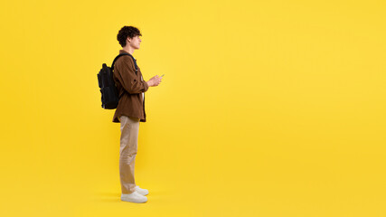 Fototapeta na wymiar Student Guy Using Smartphone Pointing Finger Aside Over Yellow Background
