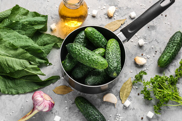 Saucepan with fresh cucumbers and ingredients for preservation on grunge background