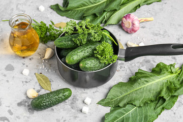 Saucepan with fresh cucumbers and ingredients for preservation on grunge background