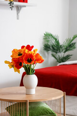 Vase with beautiful tulip flowers on wooden table in interior of bedroom