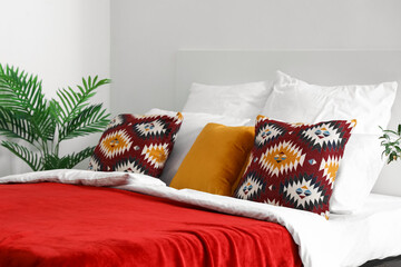 Cozy bed with pillows and red blanket in interior of bedroom