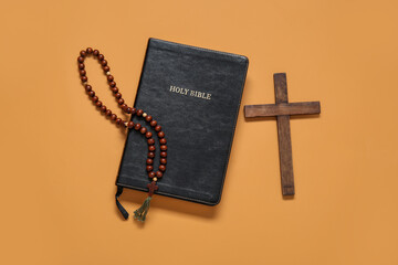 Holy Bible with cross and prayer beads on orange background