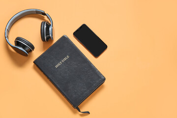 Holy Bible with earphones and smartphone on orange background