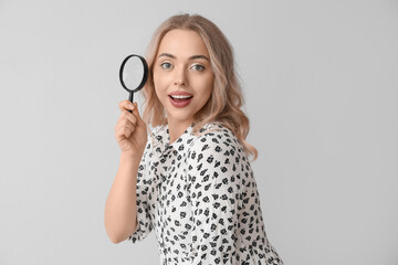 Young woman with magnifier on light background