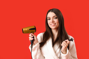 Beautiful young woman with hair dryer on red background