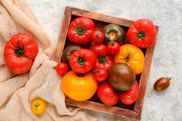 Wooden box with different fresh tomatoes on grey background